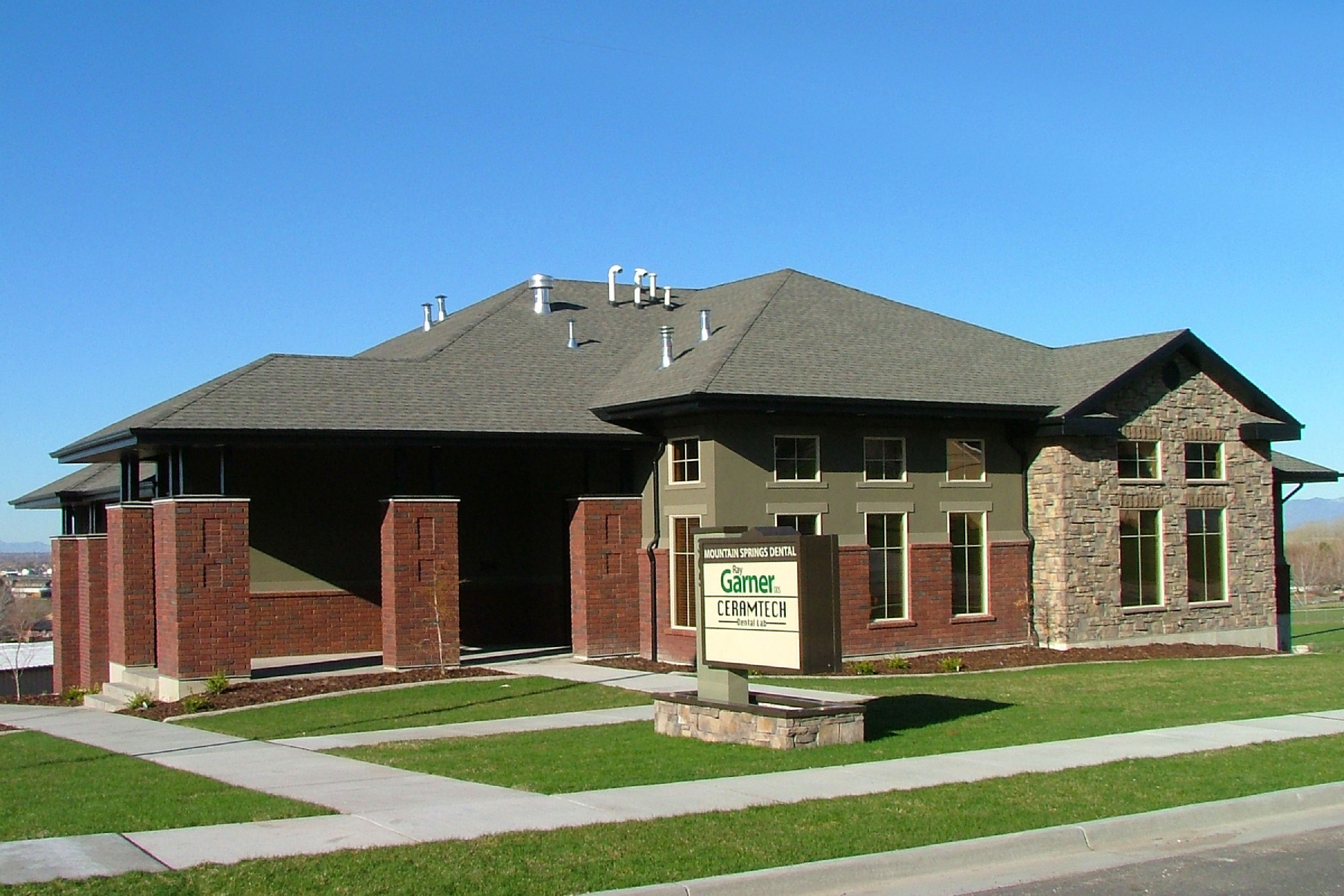 Brick and stone dental office building with a Mountain Springs Dental and Ceramtech Dental Lab sign on the front lawn under a clear blue sky